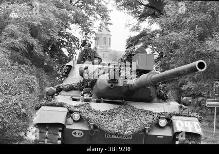 Army Exercise Atlantic Lion Germany Army, Whizgle News, Dutch Desk, Niederlande, 1950 - 2000 am 20-09-1983. Diese Themen werden in der Abbildung angezeigt. Die Szene zeigt einen Militärpanzer, der im Vordergrund sichtbar ist und mit einem Tarnnetz verziert ist, das sich in die Umgebung einfügt. Die Oberfläche des Tanks ist durch gedämpfte Grün-, Braun- und Schwarztöne gekennzeichnet, die die Texturen von Laub und Erde nachahmen. Auf dem Panzer sitzen mehrere Soldaten, die in Militäruniformen mit Helmen gekleidet sind. Ihre Ausdrucksformen sind fokussiert und spiegeln ein Gefühl von Pflicht und Wachheit wider, während sie aufsteigen Stockfoto