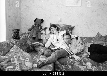 Ellen & Gerard sind zusammen Junggesellen IJm. IJmuiden the Netherlands, Whizgle News, Dutch Desk, Niederlande, 1950 - 2000 am 12-12-1996. Die Abbildung zeigt diese Themen. In einer gemütlichen Einrichtung entspannt sich ein junges Paar auf einer gemusterten, leicht abgenutzten Couch, die eine Mischung aus abstrakten Formen in Blau-, Grün- und Grautönen aufweist. Die Frau, in einer weißen Jacke gekleidet, lehnt sich zurück, ihr Ausdruck nachdenklich, während sie mit gestrecktem Arm zur Seite blickt. Der Mann, der ein lässiges helles Hemd trägt, lehnt sich gegen sie und wirkt entspannt, aber verlobt mit ihrer Anwesenheit. Dahinter stehen farbenfrohe s Stockfoto