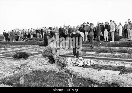 Gedenken an Hannie Schaft auf dem Ehrenfriedhof Bloemendaal, Whizgle News, Dutch Desk, Niederlande, 1950 - 2000 am 01-12-1984. Diese Themen werden in der Abbildung angezeigt. Die Szene zeigt eine düstere Zusammenkunft auf einem Friedhof mit einer Gruppe von Menschen im Hintergrund. Sie tragen dunkle Kleidung in verschiedenen Farben, was ein Gefühl der Trauer oder Erinnerung andeutet, wenn sie ruhig stehen, einige mit geneigten Köpfen. Im Vordergrund liegen zwei Individuen in der Nähe eines frisch arrangierten Blumenstraußes auf dem Boden. Einer ist die Sicherung der Blumenkredite, die sanfte Anpassung der Blumen, Stockfoto