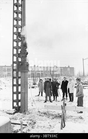 Erster Beitrag Santpoort erster Beitrag, Whizgle News, Dutch Desk, Niederlande, 1950 - 2000 am 08-12-1969. Diese Themen werden in der Abbildung angezeigt. Die Szene fängt eine Gruppe von acht Personen in einer verschneiten Umgebung im Freien ein und zeigt einen Moment, der sich auf ein hoch aufragendes Bohrfahrzeug konzentriert. Das Bohrfahrzeug im metallischen und industriellen Look strahlt Dampf aus und vermittelt ein Gefühl von Aktivität und Zweck. Um ihn herum ist der Boden mit einer dicken Schicht weißen Schnees bedeckt, die sich von den dunkleren Farben der Maschinen abhebt. Die Individuen, gekleidet in einer Mischung aus schweren Mänteln und Kleidung für den Winter in verschiedenen Farben – dunkel Stockfoto
