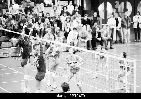 Ovra - Delta Lloyd Ladies Volleyball, Whizgle News, Dutch Desk, Niederlande, 1950 - 2000 am 24-10-1987. Das Bild enthält diese Themen. Die Szene fängt einen dynamischen Moment in einem Volleyballspiel ein, das in einem belebten Sportraum voller Zuschauer spielt. Der Platz ist mit hellen Linien gekennzeichnet, die sich vom glatten, polierten Holzboden abheben und dem Geschehen ein Gefühl der Ordnung verleihen. Im Vordergrund stehen zwei Spieler in einem angespannten Moment im Netz. Eine Athletin, die eine dunkle Uniform mit der Nummer 9 trägt, springt anmutig, um einen eingehenden Ball zu blockieren, die Arme hoch über ihr er gestreckt sind Stockfoto