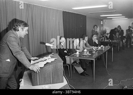 Präsentation des Buches 'Help we are developed' The Hague Nieuwspoort Spectrum, Whizgle News, Dutch Desk, Niederlande, 1950 - 2000 am 14-03-1978. Diese Themen sind in der Abbildung dargestellt. In einem geräumigen Raum mit gedämpfter Farbpalette versammelt sich eine Gruppe von Einzelpersonen. Die Einrichtung verfügt über eine professionelle Atmosphäre, die durch eine sanfte Deckenbeleuchtung verstärkt wird, die ein warmes Leuchten erzeugt. Ganz vorne steht ein Mann selbstbewusst hinter einem hölzernen Podium, das mit einem Mikrofon verziert ist. Er trägt einen maßgeschneiderten Anzug und spricht mit ausdrucksvollen Gesten an das Publikum. Seine Haltung deutet auf Autorität hin, und er Stockfoto
