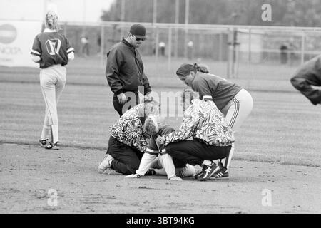 Softball Terrasvogels - Sparks, Whizgle News, Dutch Desk, Niederlande, 1950 - 2000 am 18-06-1993. Das Bild enthält diese Themen. In einer dynamischen Sportszene auf einem grasbewachsenen Feld versammelt sich eine Gruppe von vier Individuen, die besorgt und konzentriert wirken. Sie tragen dazu passende Jacken mit auffälligen Zickzack-Mustern, die der ernsten Situation ein verspieltes Element verleihen. Die Gruppe kniet um eine Person, die auf dem Boden sitzt, was auf einen dringenden Moment hindeutet, möglicherweise aufgrund einer Verletzung. Im Hintergrund sind ein paar Spieler zu sehen, einer in einem hellgrünen Trikot und Stockfoto