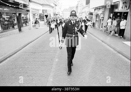 25 Musikbands und Miss majorette Zandvoort Music Zandvoort, Whizgle News, Dutch Desk, Niederlande, 1950 - 2000 am 12-05-1985. Dies sind die Themen im Bild. Die Szene zeigt eine belebte Straße, die von einer Prozession durchzogen wird. Eine Figur in formeller schwarzer Uniform, die mit silbernen Verzierungen und einem unverwechselbaren Hut verziert ist, führt mit einem Hauch von Autorität den Weg. Er hält ein zeremonielles Schwert in einer Hand, und sein Ausdruck vermittelt eine Mischung aus Stolz und Fokus. Um ihn herum folgt eine Gruppe ähnlich gekleideter Individuen, die jeweils eine passende Uniform tragen, die ein Gefühl der Einheit anzeigt Stockfoto