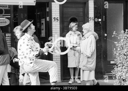 Clowns verteilt Spekulationen in der Einkaufsstraße Generaal Cronjéstraat Haarlem, Whizgle News, Dutch Desk, Niederlande, 1950 - 2000 am 20.09.1996. Die Abbildung zeigt diese Themen. In einer lebhaften urbanen Umgebung entfaltet sich die Szene mit spielerischer Energie. Auf der linken Seite jongliert ein Darsteller in einem gepunkteten Kostüm mit mehreren Ringen, sein Ausdruck ist animiert und fesselnd und zeigt sein Können mit einem charmanten Lächeln. Die Ringe sind hell weiß und stehen in Kontrast zu den tiefen Tönen seines Outfits. In der Nähe ist eine kleine Gruppe von Zuschauern von seinem Auftritt fasziniert. Ein Kind mit zerzausten Haaren steht am f Stockfoto