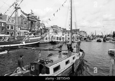 Sonstiges Sailing Days Haarlem the Netherlands, Whizgle News, Dutch Desk, Niederlande, 1950 - 2000 am 11-09-1992. Die Abbildung zeigt diese Themen. Die Szene zeigt eine geschäftige Uferpromenade mit einer Reihe von Booten, die entlang eines sanft fließenden Kanals angedockt sind. Es gibt eine Vielzahl von Schiffen, von kleinen Segelbooten bis hin zu größeren Freizeityachten, die alle friedlich auf der Wasseroberfläche ruhen. Die Architektur am Ufer des Kanals zeigt bezaubernde Gebäude mit unterschiedlichen Giebeldächern, die in hellen Farbtönen gestrichen sind, die den bewölkten Himmel ergänzen. Viele Strukturen haben dekorative Elemente, wie z. B. Stockfoto
