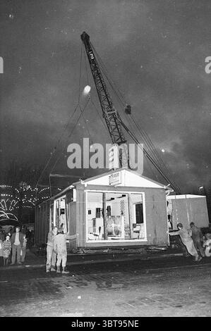Umzug des Büros Orion. Work, Whizgle News, Dutch Desk, Niederlande, 1950 - 2000 am 01-12-1970. Die Abbildung zeigt diese Themen. Die Szene spielt während der Dämmerung und zeichnet sich durch einen stimmungsvollen, bewölkten Himmel aus, der ein dimmes Licht über die Gegend wirft. Ein großer Baukran dominiert den Vordergrund, der über der Szene thront und seinen Arm zu einem neu installierten Bauwerk hin streckt. Die metallische Oberfläche des Krans ist stark gegen die düsteren Wolken, mit Reflektionen, die das verblassende Licht einfangen. Im Zentrum befindet sich ein teilweise errichtetes Gebäude, dessen Wände in gedämpften Grautönen gestrichen sind. Windows, viele davon Stockfoto