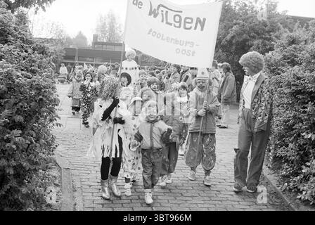School de Wilgen Moves Hoofddorp (Kinder als Clowns gekleidet) Hoofddorp the Netherlands, Whizgle News, Dutch Desk, Niederlande, 1950 - 2000 am 10-05-1992. Das Bild enthält diese Themen. Eine lebhafte Szene entfaltet sich in einer fröhlichen Umgebung im Freien, in der eine Gruppe von Kindern und Erwachsenen fröhlich parade. Die Kinder, eine Mischung aus Jungen und Mädchen, tragen farbenfrohe Clown-Kostüme. Jedes Outfit zeigt eine Vielzahl von lebendigen Mustern und Farbtönen – Polka Dots, Streifen und Glitzer. Ihre Gesichter sind mit hellen, skurrilen Motiven bemalt, die von einem breiten Lächeln bis zu verspielten Formen reichen und eine Atmosphäre verleihen Stockfoto