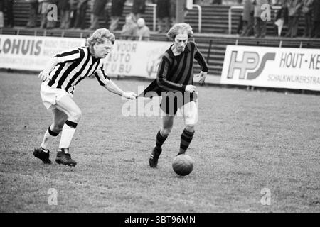 EDO - VUC Football EDO, Whizgle News, Dutch Desk, Niederlande, 1950 - 2000 am 22-01-1977. Die Abbildung zeigt diese Themen. Auf einem pulsierenden Sportfeld stehen zwei Spieler in einem intensiven Wettkampf. Ein Spieler, der ein schwarz-rot gestreiftes Trikot trägt, dribbelt einen Fußball, während sein Gegner in einem schwarz-weiß gestreiften Outfit hinter ihm her sprintet und nach hinten greift, um wieder in Besitz zu kommen. Das grasbewachsene Feld wird durch natürliches Tageslicht beleuchtet und erzeugt sanfte Schatten, die die dynamische Bewegung der Spieler verbessern. Die Komponente Umgebung Stockfoto