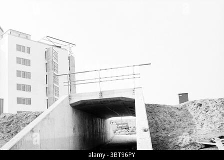 Tunnel in der Wohnung Velserbroek, Whizgle News, Dutch Desk, Niederlande, 1950 - 2000 am 23-03-1995. Die Abbildung zeigt diese Themen. Die Szene zeigt eine städtische Baustelle, die von einer harten und industriellen Atmosphäre geprägt ist. Ein Betontunnel oder eine Unterführung dominiert den Vordergrund, wobei glatte, graue Oberflächen im Kontrast zu den rauen, erdigen Tönen des umgebenden Bodens und Kies stehen. Diese solide Struktur führt zu einem weiter entwickelten Bereich darüber hinaus. Auf der linken Seite steht ein modernes Gebäude mit einer leeren Fassade, dessen Design eine Reihe von großen rechteckigen Fenstern aufweist, die das Umgebungslicht einfangen. Stockfoto