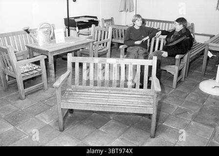 Weide und Dansik Jugendverein Appelaar Jugend- und Jugendspiele Gesellschaft Haarlem Appelaarsteeg Niederlande, Whizgle News, Dutch Desk, Niederlande, 1950 - 2000 am 24-03-1989. Dies sind die Themen im Bild. Die Szene bietet eine gemütliche Inneneinrichtung mit rustikalem Charme, gekennzeichnet durch Holzbänke, die in einer Konversationskonfiguration angeordnet sind. Zwei Personen besetzen diesen Raum, sitzen auf einer Bank und unterhalten sich. Die Bänke sind schlicht und doch elegant, aus hellem Holz gefertigt und mit Lattenmotiven, die zur Luft hin offen sind, sorgen für ein harmonisches, natürliches Gefühl. Ein runder Holztisch sitzt ne Stockfoto