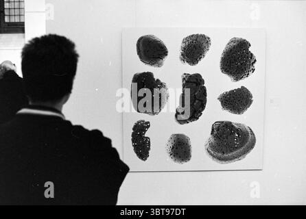 Art in the Vleeshal Haarlem Grote Markt The Netherlands, Whizgle News, Dutch Desk, Niederlande, 1950 - 2000 am 04-02-1993. Das Bild enthält diese Themen. Die Szene zeigt eine zeitgenössische Kunstgalerie mit einem Schwerpunkt auf einem eindrucksvollen abstrakten Kunstwerk, das auf einer weißen Wand positioniert ist. Das Kunstwerk besteht aus unregelmäßigen Formen und Klumpen, die sich in Größe und Textur unterscheiden und in einer monochromatischen Palette präsentiert werden, die überwiegend tiefschwarz mit Anklängen von Grau und subtilen Glanzlichtern ist. Diese Formen wirken fast organisch und ähneln natürlichen Elementen oder Texturen, die zur Besinnung anregen. Im Vordergrund: A Stockfoto