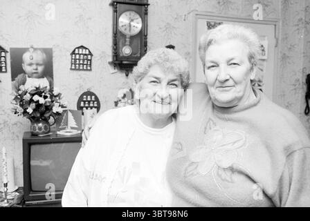 Frau Bencharski Haarlem Niederlande, Whizgle News, Dutch Desk, Niederlande, 1950 - 2000 am 20-12-1993. Dies sind die Themen im Bild. Die Szene zeigt zwei ältere Frauen, die eng zusammen stehen und ein warmes und liebevolles Lächeln zeigen. Ihr weiches, lockiges Haar ist grau, und ihre Gesichter zeigen die sanften Linien, die mit dem Alter einhergehen, was auf ein Leben voller gemeinsamer Erfahrungen hindeutet. Eine Frau trägt einen hellen Cardigan über einem gemusterten Pullover, während die andere in einen gemütlichen, verzierten Pullover mit Blumenmuster gekleidet ist. Ihre Kleidung strahlt Komfort und Nostalgie aus, was betont Stockfoto