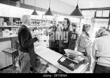 Interview mit Jaap Tanis Haarlem Smedestraat Niederlande, Whizgle News, Dutch Desk, Niederlande, 1950 - 2000 am 18.03.1989. Das Bild enthält diese Themen. In einem geschäftigen Geschäft fängt die Szene einen Moment der lebhaften Interaktion zwischen mehreren Personen ein. An der Spitze steht ein älterer Mann mit hellen Haaren hinter einer Theke und spricht mit zwei Kunden an. Sein Verhalten deutet auf Wärme und Vertrautheit hin, während er anscheinend lächelt und aufmerksam zuhört. Einer der Kunden, ein Mann mit Schnurrbart und dunklen Haaren, scheint animiert zu sein und erzählt möglicherweise eine Geschichte oder stellt eine Frage. Er ich Stockfoto