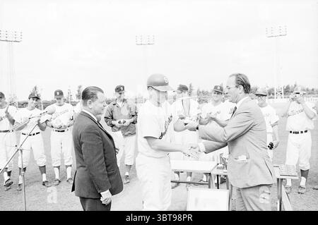 Preisverleihung Sullivans and Others Baseball Awards Ceremony, Whizgle News, Dutch Desk, Niederlande, 1950 - 2000 am 28.07.1968. Die Abbildung zeigt diese Themen. Die Szene fängt einen Moment auf einem Baseballfeld ein, wo eine Zeremonie stattfindet. Im Vordergrund befinden sich zwei Hauptfiguren, die an einem Handschlag beteiligt sind. Der eine ist ein junger Athlet in einer weißen Baseballuniform mit einer Kappe, was darauf hindeutet, dass er ein Spieler ist, der eine Auszeichnung oder Anerkennung erhält. Er steht aufrecht und strahlt ein Gefühl von Stolz und Leistung aus. Die zweite Figur ist ein gut gekleideter Mann, der einen Anzug trägt, wahrscheinlich ein Würdenträger oder von Stockfoto