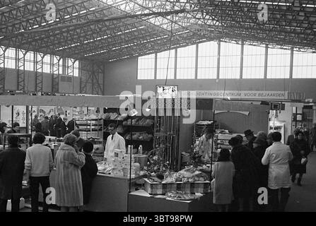 Eröffnung der Frühjahrsmesse Spring Fair, Whizgle News, Dutch Desk, Niederlande, 1950 - 2000 am 29-02-1968. Diese Themen werden in der Abbildung angezeigt. Die Szene zeigt ein geschäftiges Marktumfeld, das sich durch einen großen, offenen Raum mit verschiedenen Ständen auszeichnet. Die hohe Decke besteht aus Metallbalken, die viel natürliches Licht durch großzügige Fenster einströmen lassen und eine helle und luftige Atmosphäre im gesamten Bereich schaffen. Im Vordergrund versammelt sich eine Gruppe von Personen um einen Stand, der eine Reihe von Waren zeigt. Der Stand hat eine breite Arbeitsplatte, die mit einer ordentlichen Dekoration verziert ist Stockfoto