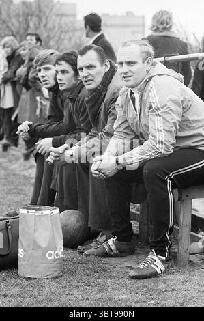 Coach-Verwalter eines Fußballvereins., Whizgle News, Dutch Desk, Niederlande, 1950 - 2000. Dies sind die Themen im Bild. In einer lebhaften Umgebung im Freien sitzt eine Gruppe von vier Personen auf niedrigen Holzbänken und beobachtet ein Fußballspiel im Hintergrund. Die Szene ist von einer Mischung aus Vorfreude und Kameradschaft erfüllt, da die Zuschauer in der Gegend verstreut sind. Die vier Individuen tragen verschiedene Kleidung; zwei Männer in dunklerer Kleidung, die wahrscheinlich einen formelleren oder professionelleren Look repräsentieren, sitzen eng zusammen. Der dritte Mann, leicht abgewandt, hat mehr Ca Stockfoto