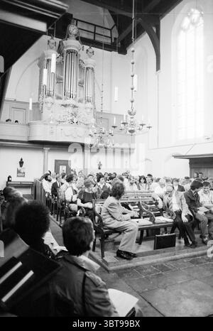 Orgelspiele Wallonische Kirchenorgeln und Organisten, Whizgle News, Dutch Desk, Niederlande, 1950 - 2000 am 29.07.1988. Dies sind die Themen im Bild. Die Szene befindet sich in einer geräumigen, gut beleuchteten Kirche, die sich durch hohe gewölbte Decken und hohe, bogenförmige Fenster auszeichnet, die natürliches Licht einströmen lassen. Die Atmosphäre ist ruhig und besinnlich, geprägt von Ehrfurcht. In ordentlichen Reihen sitzen mehrere Personen, die überwiegend in formeller oder halbformaler Kleidung gekleidet sind. Das Publikum scheint aufmerksam und engagiert zu sein, was darauf hindeutet, dass es an einem wichtigen Ereignis teilnehmen könnte Stockfoto