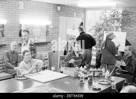 Residents Hartenkamp Bennebroek Bennebroek, Whizgle News, Dutch Desk, Niederlande, 1950 - 2000 am 26-11-1995. Diese Themen sind in der Abbildung dargestellt. Die Szene fängt einen belebten Kunstraum in einer warmen, einladenden Atmosphäre ein. Die weiche, diffuse Beleuchtung von obenliegenden Leuchtstofflampen erhellt den Raum, beleuchtet verschiedene Aktivitäten und schafft eine lebhafte und dennoch entspannte Stimmung. Im Vordergrund steht ein langer Tisch mit Kunstvorräten: Farbgläser in verschiedenen Farben und Pinsel in Behältern. Ein paar Schüsseln, vielleicht zum Mischen von Farben, sitzen in der Nähe, um das künstlerische zu verstärken Stockfoto