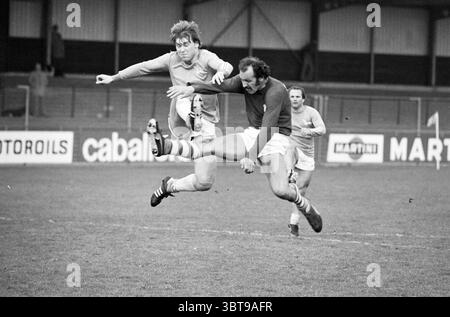 Fußballfinale IJmuiden: Stormvogels - VSV Football V.S.V. Velsen Stormvogels, Whizgle News, Dutch Desk, Niederlande, 1950 - 2000 am 10.05.1977. Diese Themen sind in der Abbildung dargestellt. In der Szene werden zwei Spieler mitten in einem intensiven Moment auf einem grasbewachsenen Feld gefangen, was auf ein Fußballspiel hindeutet. Ein Spieler, der eine helle Uniform trägt, befindet sich in der Luft und hüpft eindrucksvoll, um einem gegnerischen Spieler auszuweichen. Sein Haar ist von der Action abgewühlt, und sein Ausdruck ist fokussiert, wenn er versucht, die Herausforderung zu überwinden. Der zweite Spieler, der in einer dunkleren Uniform gekleidet ist, scheint es zu tun Stockfoto