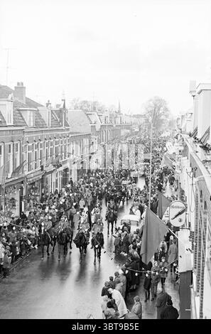 Sinterklaas' Ankunft Haarlem Generaal Cronjéstraat the Netherlands., Whizgle News, Dutch Desk, Niederlande, 1950 - 2000. Diese Themen werden in der Abbildung angezeigt. Die Szene fängt ein lebhaftes Straßentreffen voller Menschen ein. Eine geschäftige Menschenmenge füllt die enge Straße, die von traditionellen Gebäuden auf beiden Seiten gesäumt ist, deren Architektur eine Mischung aus Stilen aufweist, vielleicht mit Markisen und dekorativen Fassaden. Die Atmosphäre ist lebhaft, aber etwas gedämpft, verstärkt durch den bewölkten Himmel, der die Szene bedeckt und ein weiches, diffuses Licht erzeugt, das der geschäftigen Umgebung eine ruhige Atmosphäre verleiht. In Stockfoto