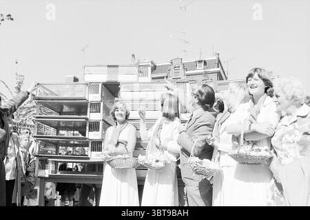 Eröffnung der NZH-Station Haarlem Noord Zuid Hollandse Vervoersmaatschappij N.V. NZ Eröffnung der Öffnungen Inbetriebnahme, Whizgle News, Dutch Desk, Niederlande, 1950 - 2000 am 11-06-1977. Die Abbildung zeigt diese Themen. In einer lebhaften Outdoor-Szene stehen mehrere Frauen im Vordergrund, alle in eleganten, hellen Kleidern, die ein Gefühl von Feiern widerspiegeln. Ihr Ausdruck ist fröhlich, mit Lächeln und Lachen unter ihnen, was zu einer fröhlichen Atmosphäre beiträgt. Einige der Frauen halten Korbkörbe mit Blumen, die einen Hauch Wärme und eine Verbindung zur Natur verleihen. Dahinter steht ein Stockfoto