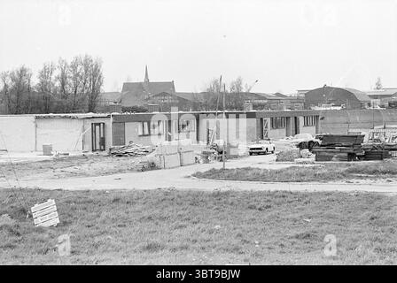 Construction Houses Hoofddorp Construction sites, Whizgle News, Dutch Desk, Niederlande, 1950 - 2000 am 08-05-1969. Das Bild enthält diese Themen. Die Szene zeigt eine Baustelle vor einem Hintergrund gedämpfter, bedeckter Himmel, der der gesamten Komposition einen grauen Ton verleiht. Im Vordergrund gibt es eine weite Fläche von ungezähmtem Gras, dessen stumpfes Grün mit braunen Flecken verschmolzen ist, was darauf hindeutet, dass das Gebiet noch nicht vollständig erschlossen ist. Auf der linken Seite sind Stapel von Baumaterialien, einschließlich Ziegeln und Bauholz, übersichtlich angeordnet, was auf die laufenden Bauarbeiten hindeutet Stockfoto