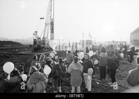 Erster Stapel der Ark Velserbroek, Whizgle News, Dutch Desk, Niederlande, 1950 - 2000 am 28.11.1991. Die Abbildung zeigt diese Themen. Auf einer kargen Baustelle erhebt sich im Hintergrund ein großer Kran, dessen imposante Struktur sich vor einem hellen, trüben Himmel schmiegt. Die Szene ist gefüllt mit einer vielfältigen Gruppe von Menschen, vor allem Kindern, die sich in Clustern versammelt haben. Sie halten weiße Ballons, die nach oben schweben und die Erdtöne des matschigen Bodens unter ihnen kontrastieren. Die Menge ist in lässiger Winterkleidung gekleidet; viele tragen Jacken mit Kapuze, einige haben sogar bunte Tücher, die um sie gewickelt sind Stockfoto