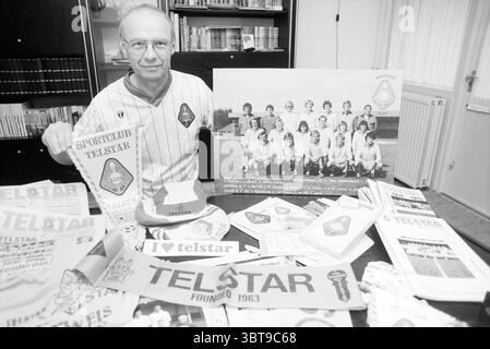 Herr Heideman Telstarfan B'wijk Beverwijk Niederlande, Whizgle News, Dutch Desk, Niederlande, 1950 - 2000 am 09.09.1996. Das Bild enthält diese Themen. Die Szene zeigt eine Person an einem Tisch, umgeben von einer Sammlung von Erinnerungsstücken zu einem Sportclub. Die Person trägt ein helles Trikot, was auf eine Verbindung zum Club hindeutet. Ihr Ausdruck spiegelt ein Gefühl von Stolz und Nostalgie wider. Der Tisch ist überfüllt mit verschiedenen Gegenständen wie Bannern, Broschüren und Fotos, die alle eine reiche Geschichte des Clubs zeigen. Die Farben der Erinnerungsstücke reichen von Stockfoto