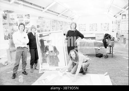 Organisation einschließlich Harm Botman Fotoausstellung Spaarne Archive Photography, Whizgle News, Dutch Desk, Niederlande, 1950 - 2000 am 26-08-1986. Dies sind die Themen im Bild. In einer geräumigen, gut beleuchteten Galerie versammeln sich vier Personen um ein großes, Vintage-Foto, das eine Person mit einer Kamera zeigt. Die Atmosphäre ist kollaborativ und kreativ, denn künstlerische Projekte und Fotografie sind überall im Raum verstreut. Die erste Person links, die ein weißes Langarmhemd und eine dunkle Hose trägt, hat einen engagierten Ausdruck, der möglicherweise eine Idee oder ein Konzept erklärt. Ne Stockfoto