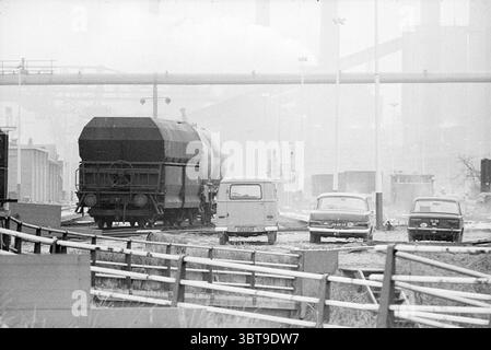 Eisenbahnstreik Hoogovens Hoogovens, Whizgle News, Dutch Desk, Niederlande, 1950 - 2000 am 16-12-1969. Dies sind die Elemente im Bild. Die Szene fängt eine Industrielandschaft ein, die von einer nebeligen, bewölkten Atmosphäre geprägt ist. Ein Bahngleis führt diagonal durch das Zentrum, das zu einem großen, zylindrischen Güterwagen führt, der den Vordergrund dominiert. Dieses Auto ist in einem gedämpften Ton lackiert und hat eine schwere, dunkle Abdeckung, die auf den Transport von Schüttgütern hindeutet. Rund um die Bahnstrecke können mehrere Fahrzeuge zufällig geparkt werden. Unter ihnen zeichnet sich ein Kastenwagen aus, der sich durch sein l Stockfoto