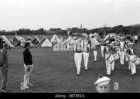 6 Tage IJmuiden. Strand und Strände Wandern, Whizgle News, Dutch Desk, Niederlande, 1950 - 2000 auf 31-07-1963. Diese Themen werden in der Abbildung angezeigt. Die Szene fängt ein lebhaftes Outdoor-Event auf einem gepflegten Grasfeld ein. Im Vordergrund marschiert eine Gruppe junger Musiker im Einklang. Jedes Mitglied trägt weiße Hosen und eine knackige Uniform mit Hüten. Sie tragen Trommeln, die beim marsch und Spielen besonders hervorgehoben werden, wodurch ein Gefühl von Rhythmus und Energie entsteht. Links und rechts sind mehrere Zelte aufgestellt, was auf ein Campingelement für die Versammlung hindeutet. Die Zelte variieren in Größe und Höhe Stockfoto