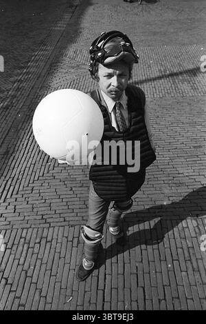 Louis Ferron mit Ballpersonen, Whizgle News, Dutch Desk, Niederlande, 1950 - 2000 am 13.09.1968. Diese Themen werden in der Abbildung angezeigt. Die Szene zeigt eine einzigartige Figur, die auf einer strukturierten Backsteinoberfläche steht, wahrscheinlich auf einem Bürgersteig oder einem Außenbereich. Die Person trägt ein spezielles Outfit, bestehend aus einem maßgeschneiderten Anzug und einem ungewöhnlichen Schutzausrüstung-Set, das eine gepolsterte Weste und dicke Knieschoner umfasst, was eine Mischung aus formeller und sportlicher Ästhetik suggeriert. Ihr Kopf ist mit einem helmähnlichen Accessoire verziert, das der Szene ein verspieltes oder absurdes Element verleiht. Der Ausdruck des Einzelnen ist ernst, W Stockfoto