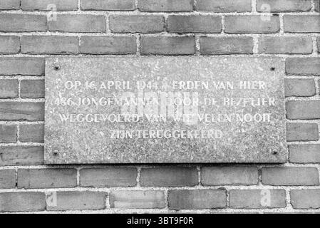 Beverwijk Station Denkmal Stein Fassade Steine Station Beverwijk Niederlande, Whizgle News, Dutch Desk, Niederlande, 1950 - 2000 am 16-12-1983. Das Bild enthält diese Themen. Die Szene zeigt eine strukturierte Ziegelwand, die hauptsächlich aus kleinen, rechteckigen Ziegeln in verschiedenen Brauntönen besteht. Die Ziegel sind in einem leicht unregelmäßigen Muster angeordnet, wobei einige Anzeichen von Alter und Witterung zeigen, was der Oberfläche einen Eindruck von Geschichte vermittelt. In der Mitte steht eine rechteckige Tafel aus verwittertem Metallmaterial im Kontrast zum Backsteinhintergrund. Die Tafel ist weniger lebhaft, scharf Stockfoto