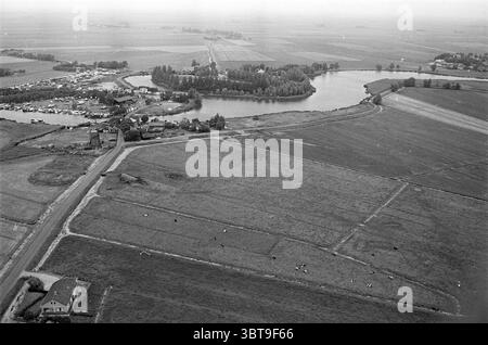 Erholungsgebiet Spaarnwoude Recreation, Whizgle News, Dutch Desk, Niederlande, 1950 - 2000 am 04-07-1975. Das Bild enthält diese Themen. Die Szene bietet einen Panoramablick auf eine ländliche Landschaft, die von ausgedehnten Feldern und einem ruhigen Gewässer geprägt ist. Die Komposition wird von einem großen, sich schlängelnden See dominiert, der von üppigen Grünflächen umgeben ist und einen markanten Kontrast zum Ackerland bildet. Die Oberfläche des Sees ist ruhig und spiegelt die gedämpften Töne des Himmels wider. Im Vordergrund erstrecken sich die Felder in verschiedenen Grün- und Brauntönen, segmentiert durch ordentliche Reihen von Feldfrüchten und PA Stockfoto