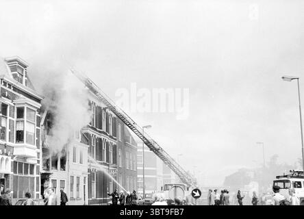 Fire Hay Market Fire Brigade Haarlem Hooimarkt the Netherlands, Whizgle News, Dutch Desk, Niederlande, 1950 - 2000 am 26-06-1980. Dies sind die Themen im Bild. Die Szene fängt einen dramatischen Moment eines städtischen Feuers ein, umgeben von einem dicken Nebel aus Rauch, der das Licht streut und eine düstere und angespannte Atmosphäre schafft. Das Gebäude, ein altes Gebäude mit Ziegelfassaden, zeigt Anzeichen von Not, während Flammen aus einem der oberen Fenster herauslecken, unbestreitbar Beweis für das Chaos im Inneren. Im Vordergrund steht eine Gruppe von Menschen in Distanz, ihre Äußerungen sind eine Mischung aus Besorgnis Stockfoto