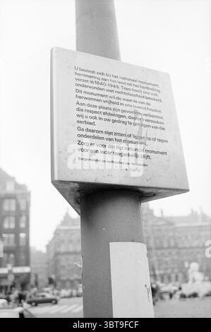 Nationales Denkmal auf dem Dam Square Amsterdam Dam the Netherlands, Whizgle News, Dutch Desk, Niederlande, 1950 - 2000 im Jahr 1973. Das Bild enthält diese Themen. Die Szene zeichnet sich durch eine schroffe, urbane Umgebung aus, die durch einen hohen, zylindrischen Pol gekennzeichnet ist, der sich im Vordergrund deutlich erhebt. Der Pfosten ist mit einer Tafel verziert, die teilweise durch den Blickwinkel verdeckt ist. Die Oberfläche der Tafel scheint hell zu sein und steht im Kontrast zu den dunkleren Tönen der Umgebung. Im Hintergrund ist eine trübe Umrisse eines großen historischen Gebäudes zu erkennen, was auf eine bedeutende Sichtweise hindeutet Stockfoto