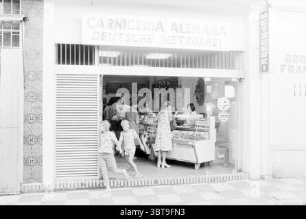 Bericht Torremolinos Spain, Whizgle News, Dutch Desk, Niederlande, 1950 - 2000 am 10-08-1978. Diese Themen sind in der Abbildung dargestellt. Die Szene befindet sich außerhalb einer malerischen Metzgerei, die sich durch ihre schlichte, einladende Fassade auszeichnet. Das Geschäft, das sich durch sein weißes Äußere und die gestreifte Markise auszeichnet, strahlt einen nostalgischen Charme aus. Eine Gruppe von Menschen versammelt sich im Inneren, die scheinbar in Gesprächen verwickelt sind, während sie verschiedene Fleischstücke auf Glaskästen untersuchen. Der Innenraum ist gut beleuchtet, sodass Sie einen freien Blick auf die sauber angeordneten Produkte wie Würstchen, Schinken und anderes Fleisch haben, die reflektieren Stockfoto