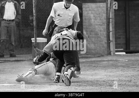 Softball Terrasvogels - Twins, Whizgle News, Dutch Desk, Niederlande, 1950 - 2000 am 11-07-1997. Die Abbildung zeigt diese Themen. Die Szene fängt einen dynamischen Moment auf einem Baseballfeld ein, der Spannung und Spannung weckt. Im Vordergrund spielen zwei Spieler ein dramatisches Spiel auf der Heimplatte. Ein Spieler, der in einem leuchtend gelben Trikot mit einer Nummer auf der Rückseite gekleidet ist, rutscht in Richtung Heimatbasis, Dreck ist um ihn herum aufgewirbelt. Ihre Haltung ist niedrig, die Arme sind ausgestreckt, um sicher an die Platte zu gelangen. Der Fänger, der ein schwarzes Jersey trägt und sich in die Hocke gebeugt hat, wirkt robust, wenn er positioniert ist Stockfoto