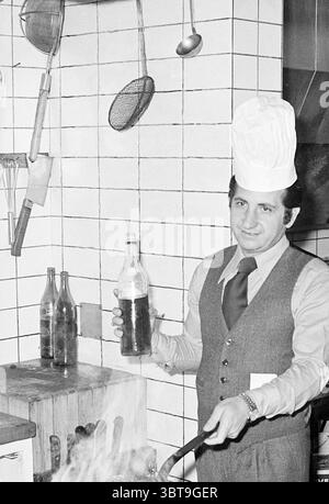 Besitzer Napoli Houtplein 10 Jahre Haarlem Essen und Restaurants Haarlem Houtplein Niederlande, Whizgle News, Dutch Desk, Niederlande, 1950 - 2000 am 08-09-1976. Das Bild enthält diese Themen. In einer belebten Küche steht ein Mann selbstbewusst und verkörpert den Geist der kulinarischen Kunst. Er trägt eine klassische Kochmütze auf dem Kopf, die sein Können signalisiert. Seine Kleidung besteht aus einer maßgeschneiderten Weste über einem Hemd mit Kragen und einer Krawatte, die Professionalität mit einem Hauch von Stil verbindet. Die Küche um ihn herum ist mit verschiedenen Utensilien und Werkzeugen gefüllt, einschließlich hängender Töpfe und Pfannen, Kreatin Stockfoto