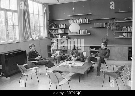 Int. Kindertagesstätte Jugendherberge Jugendherbergen, Whizgle News, Dutch Desk, Niederlande, 1950 - 2000 auf 25-03-1969. Das Bild enthält diese Themen. Die Szene präsentiert einen gemütlichen, intimen Innenraum, der sich durch eine Kombination aus Minimalismus und warmer Atmosphäre auszeichnet. Die Wände sind in gedämpften Tönen gestrichen, und die großen Fenster lassen natürliches Licht einströmen und schaffen eine sanfte Beleuchtung, die die einladende Natur des Raumes unterstreicht. Vier Personen versammeln sich um einen zentralen niedrigen Tisch aus Holz, auf dem einige Magazine und Zeitungen verteilt sind. Die Möbel sind einfach und doch funktional. Stockfoto