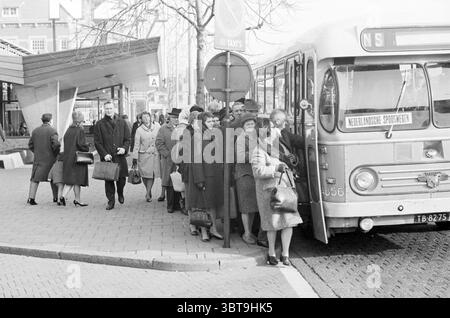 NZH-Bus wird als vorübergehender Transport für Zugpassagiere genutzt Haarlem the Netherlands., Whizgle News, Dutch Desk, Niederlande, 1950 - 2000. Diese Themen sind in der Abbildung dargestellt. An einer Bushaltestelle entfaltet sich eine geschäftige Stadtszene mit einem Gefühl von Bewegung und Aktivität. Im Vordergrund versammelt sich eine Gruppe von Einzelpersonen um einen alternden Bus, der mit geöffneter Tür geparkt wird und Passagiere zum Einsteigen einlädt. Die Menschen tragen eine Mischung aus formeller und lässiger Winterkleidung, überwiegend in Grau-, Schwarz- und Brauntönen. Viele tragen Mäntel und Hüte, was auf einen kühlen Tag hindeutet. Einige Personen halten Taschen oder sm Stockfoto