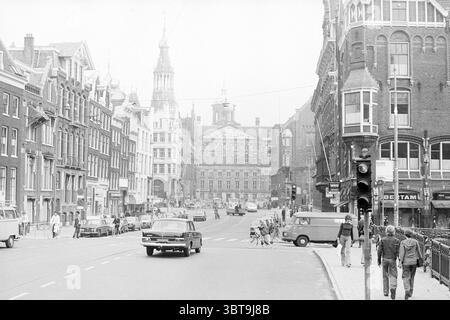 Raadhuisstr. Amsterdam mit Palaststraßen Amsterdam Raadhuisstraat Niederlande, Whizgle News, Dutch Desk, Niederlande, 1950 - 2000 am 23-09-1976. Das Bild enthält diese Themen. Die Szene fängt eine geschäftige Stadtstraße ein, gesäumt von traditioneller Architektur, die eine Mischung aus historischem und zeitgenössischem Design zeigt. Die Gebäude weisen komplexe Fassaden mit Giebeldächern und großen Fenstern auf, die in gedämpften Beige-, Braun- und Grautönen gehalten sind. Im Vordergrund ist eine breite Straße zu sehen, die zu einem zentralen Platz führt. Einige Fahrzeuge, darunter klassische Autos und Lieferwagen, sind im Einsatz Stockfoto
