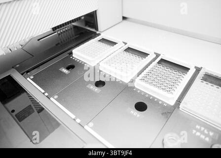HIV-Testgerät in St. Johannes de Deo Krankenhaus Haarlem Nederland, Whizgle News, Dutch Desk, Niederlande, 1950 - 2000 am 11-11-1993. Dies sind die Themen im Bild. Die Szene zeigt eine Nahaufnahme einer Laborumgebung, in der Präzision und Ordnung betont werden. Die Hauptobjekte sind mehrere rechteckige Probenteller, die ordentlich auf einer schlanken, dunklen Oberfläche angeordnet sind. Jedes Tablett enthält verschiedene Buchstaben – in einer geordneten, rasterartigen Art –, die darauf hindeuten, dass sie Teil eines systematischen Prozesses sind. Die Schalen selbst sind transparent und zeigen eine Reihe kleiner, kreisförmiger Wells, die mit einer klaren Flüssigkeit gefüllt sind. Stockfoto