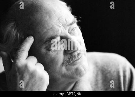 Porträt B. Droog Schauspieler, Whizgle News, Dutch Desk, Niederlande, 1950 - 2000 am 23-09-1991. Dies sind die Elemente im Bild. Die Szene fängt einen älteren Mann ein, sein Ausdruck nachdenklich und besinnlich. Sein Haar ist leicht zerzaust und grau und ergänzt die weichen Linien seines Gesichts, die Geschichten von Zeit und Erfahrung erzählen. Er hat einen klar definierten Kiefer, der mit einem Hauch von Stoppeln verziert ist, was sein Salbei-Aussehen unterstreicht. Seine Hand, teilweise auf die Stirn gehoben, deutet auf tiefes Nachdenken oder Erinnerungen hin. Die Haut scheint verwittert und zeigt das Alter anmutig. Schatten spielen über seine Gesichtszüge Stockfoto