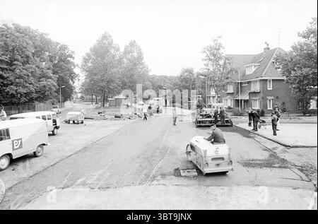 Road Works Heemstede Heemstede Road Works, Whizgle News, Dutch Desk, Niederlande, 1950 - 2000 auf 30-06-1965. Das Bild enthält diese Themen. Die Szene zeigt eine belebte Straße, die im Bau ist, gefüllt mit einer Mischung aus menschlicher Aktivität und Maschinen. Eine Gruppe von Mitarbeitern nimmt verschiedene Aufgaben wahr und demonstriert eine gemeinsame Arbeit. Einige Personen konzentrieren sich auf den Betrieb schwerer Maschinen, wie z. B. einer Pflastermaschine, während andere Materialien handhaben, die Straße pflastern oder den Bereich für weitere Arbeiten vorbereiten. Die Lage ist größtenteils Wohngebäude, mit mehreren bescheidenen Häusern entlang der Straße Stockfoto