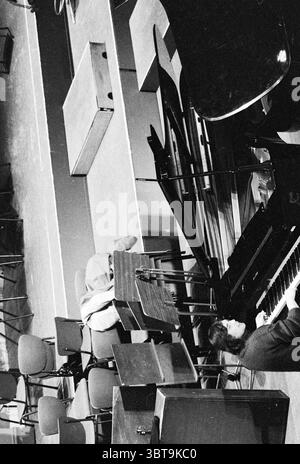 Van Kempen and Helledoorn Pianists Music, Whizgle News, Dutch Desk, Niederlande, 1950 - 2000 am 21-01-1983. Diese Themen werden in der Abbildung angezeigt. Die Szene spielt in einem geräumigen, schwach beleuchteten Raum, wahrscheinlich in einem Proben- oder Aufführungsraum. Der Boden ist mit einer glatten Oberfläche gesäumt, und die Atmosphäre lässt die Vorbereitung auf ein musikalisches Ereignis vermuten. Im Vordergrund sitzt eine Person an einem Flügel, mit den Händen über den Tasten und spielt. Die Person hat einen fokussierten Ausdruck, der die Konzentration hervorhebt, die bei ihrer Aufgabe erforderlich ist. Sie tragen ein schlichtes, dunkles Outfit, das Stockfoto