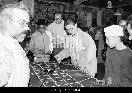 Spielsucht Themenabend IJmuiden IJmuiden the Netherlands, Whizgle News, Dutch Desk, Niederlande, 1950 - 2000 auf 30-04-1995. Dies sind die Themen im Bild. Die Szene ist voller Energie und spielt in einem lebendigen Innenraum, der von einer eklektischen Mischung aus Persönlichkeiten und Aktivitäten geprägt ist. Die Kulisse zeigt ein visuell chaotisches Arrangement von Graffiti, das helle Farben und dynamische Designs zeigt, die für eine urbane, kreative Umgebung sprechen. Im Vordergrund versammeln sich mehrere Personen um einen großen Tisch mit einem Spiellayout, der scheinbar in ein Spiel vertieft ist, das Chan beinhaltet Stockfoto