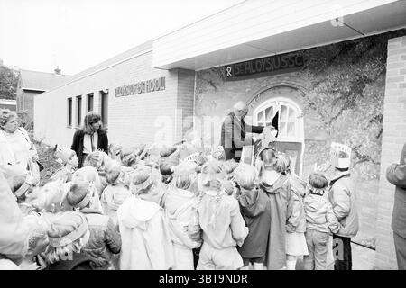 Eröffnung der Aloysiusschool Overveen Eröffnung der Öffnungen Inbetriebnahme von Overveen, Whizgle News, Dutch Desk, Niederlande, 1950 - 2000 am 16.05.1983. Dies sind die Elemente im Bild. In einer lebhaften Umgebung im Freien versammelt sich eine große Gruppe von Kindern, deren Ausdruck voller Spannung und Neugier ist. Die Kinder tragen in verspielten Kostümen bunte, gefiederte Stirnbänder, die auf einen festlichen Anlass hinweisen. Ihre Kleidung ist eine Mischung aus hellen und hellen Farben, die eine lebendige Energie ausstrahlt. Im Vordergrund steht ein erwachsener Mann in der Nähe eines Gebäudes und spricht die Menge an. Er ist in Form gekleidet Stockfoto