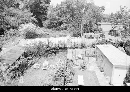 Melona Santpoort Lagerbereich Lagerbereiche Standorte Santpoort, Whizgle News, Dutch Desk, Niederlande, 1950 - 2000 am 05-07-1983. Das Bild enthält diese Themen. Die Szene präsentiert eine ruhige Umgebung im Freien, die aufgrund der monochromen Behandlung hauptsächlich in Grün- und Grautönen getaucht ist. Im Vordergrund befindet sich ein gepflegter Garten, in dem ein gepflegter Rasen von mehreren weißen Gartenstühlen unterbrochen wird, die locker angeordnet sind. Ein paar Topfpflanzen verleihen dem Grün einen Hauch von Leben. Im Hintergrund bilden eine Vielzahl von Bäumen, üppig und dicht, ein natürliches Baldachin, das zu einem Gefühl o beiträgt Stockfoto